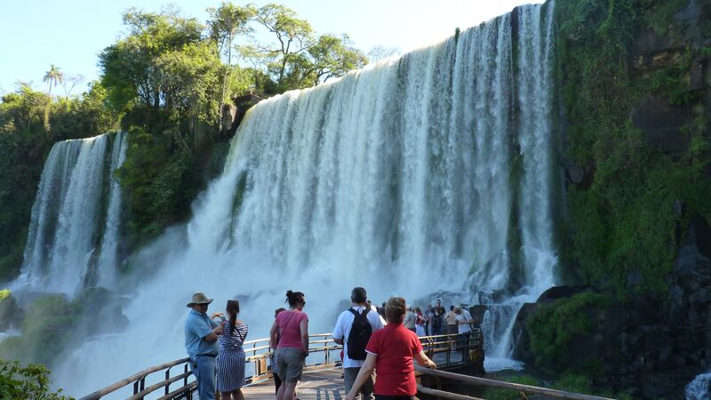 A group of travellers looking at the cascading water of one of Iguazu Falls' many waterfalls. 