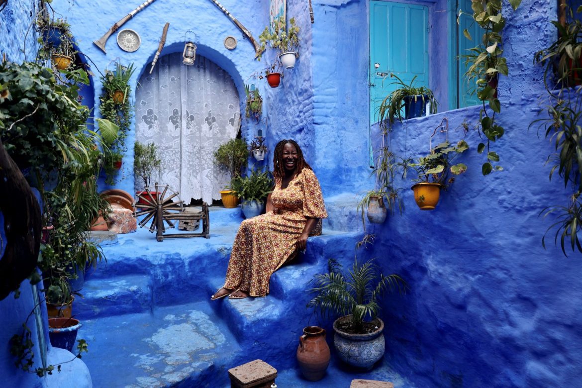 a Black woman sits in in an old blue structure of Morocco
