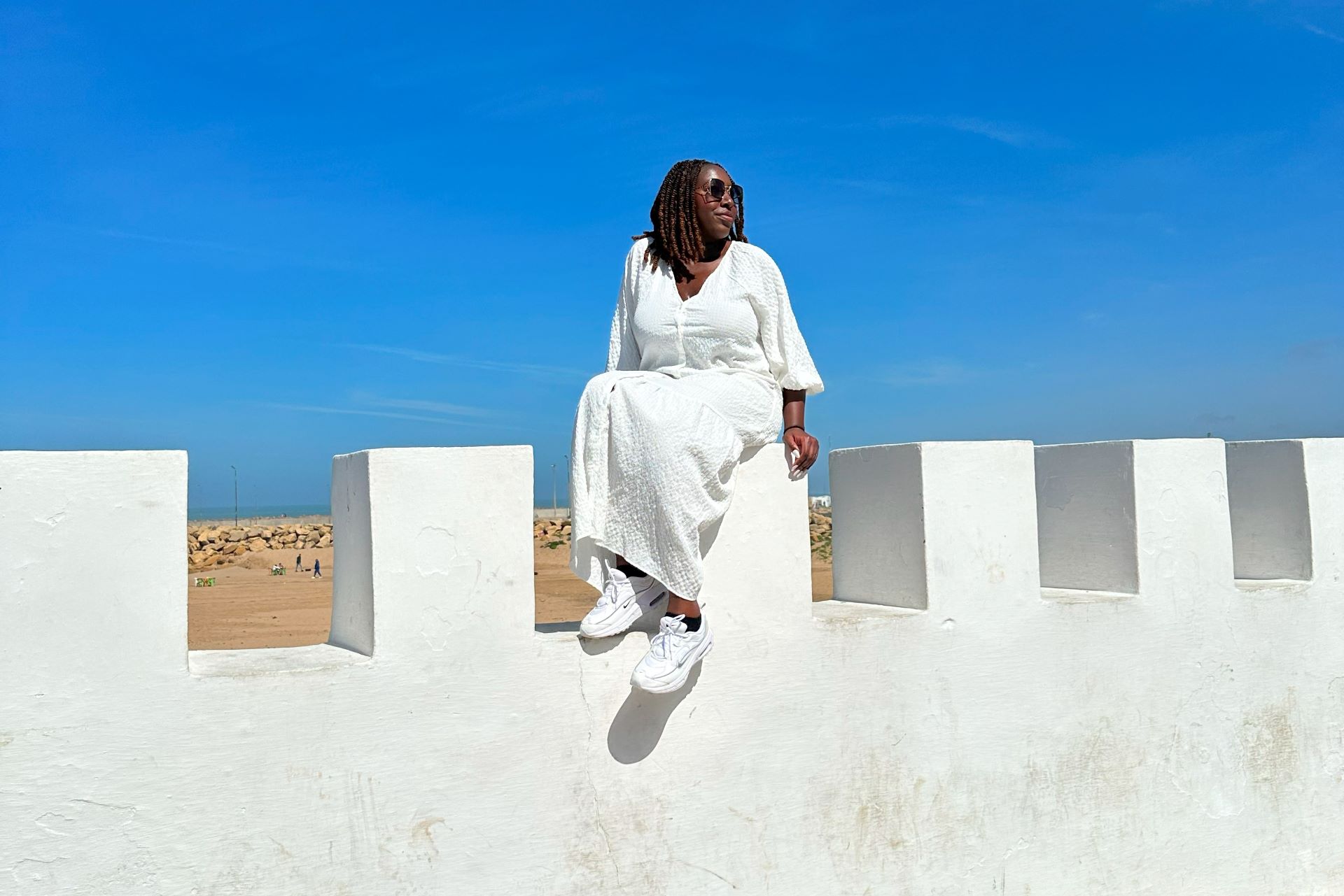 a Black woman sits perched on top of a white structure in Morocco with the desert behind her
