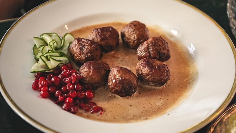 A plate of swedish meatballs with pickled cucumber and cranberry jam. 