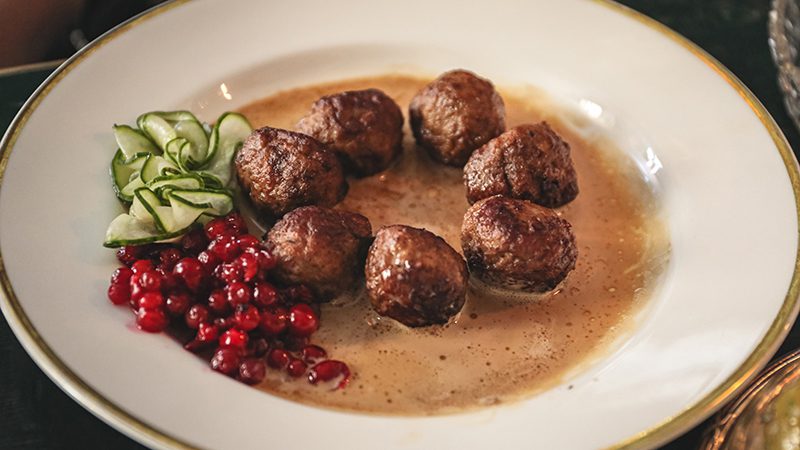 A plate of swedish meatballs with pickled cucumber and cranberry jam.