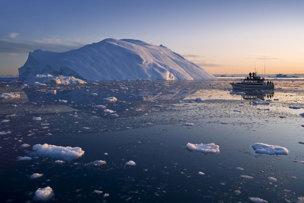 a boat sailing towards an iceberg at sunset