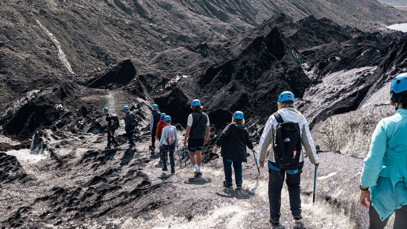 A group of travellers carefully making their way along the ash covered surface of the Solheimajokull Glacier in Iceland. 