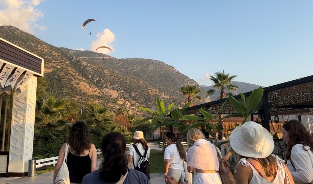 Group travellers walking through Oludeniz beach with paragliders ahead