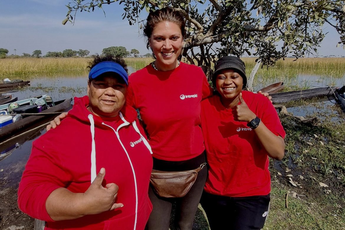 three woman in red Intrepid t-shirts with their arms around each other against a backdrop of grassy plains