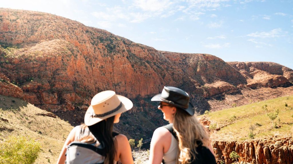 Two women sitting in the sun smiling while wearing broad-rim hats, Red Centre, Australia