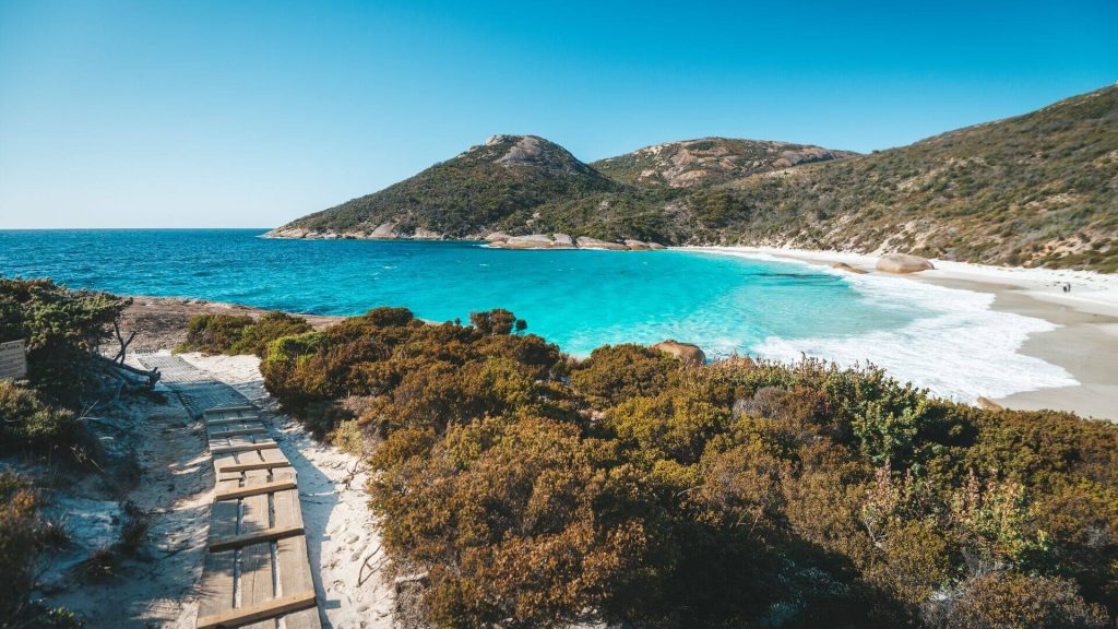 A wide shot of a beach path and wavy beach with crystal blue waters and white sand, Two Peoples Bay Nature Reserve, Western Australia 