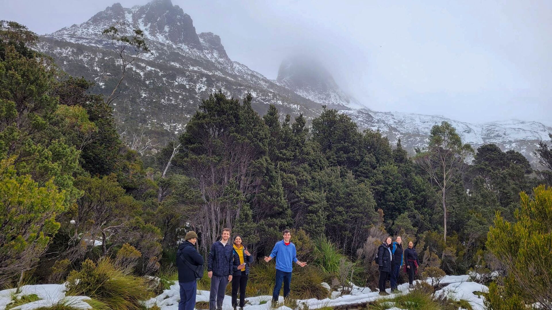A group of hikers pose on the trail surrounded by snow and Cradle Mountain.