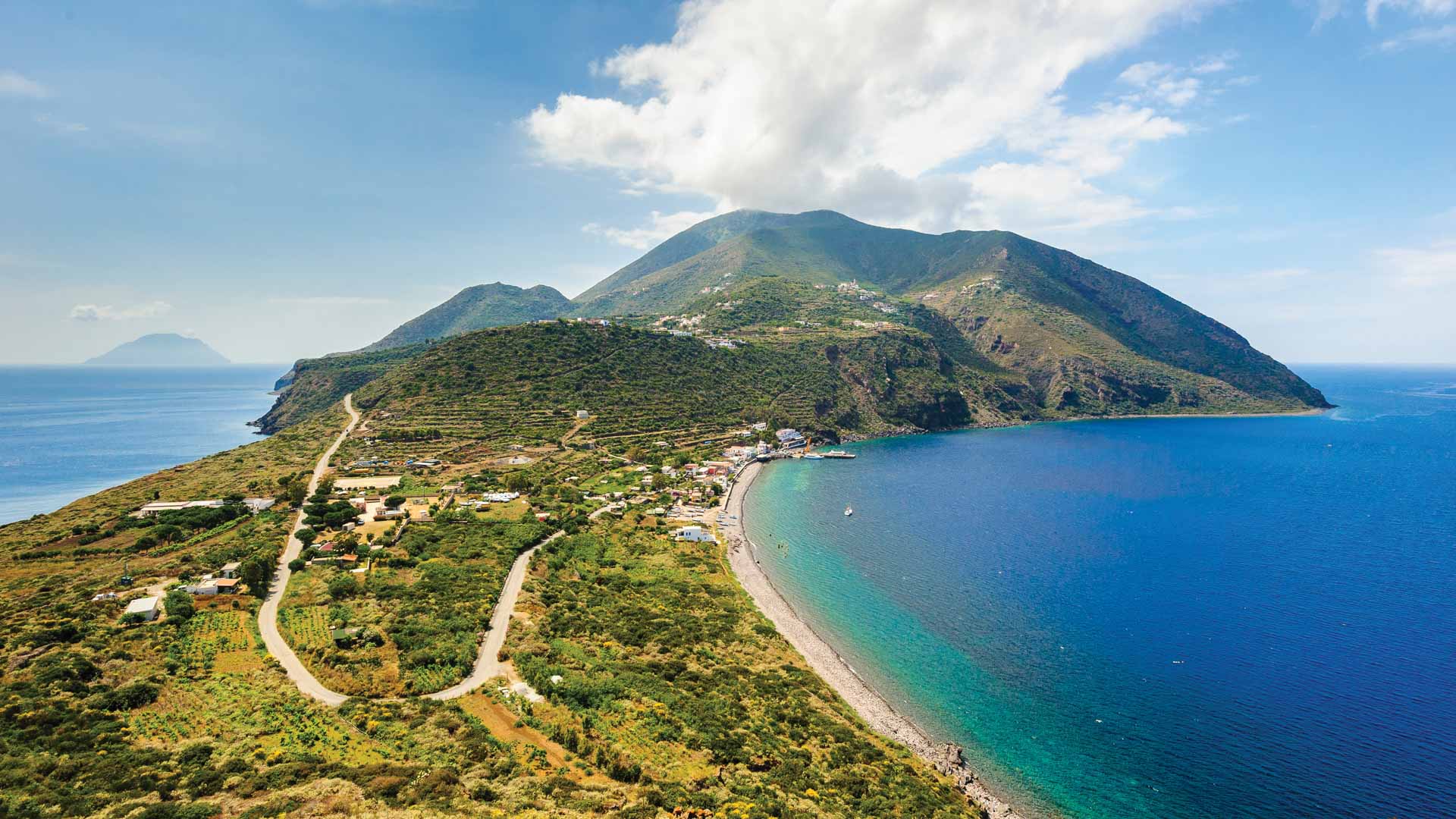 A rugged green stretch of island dotted with homes intersects an expanse of blue Mediterranean sea.