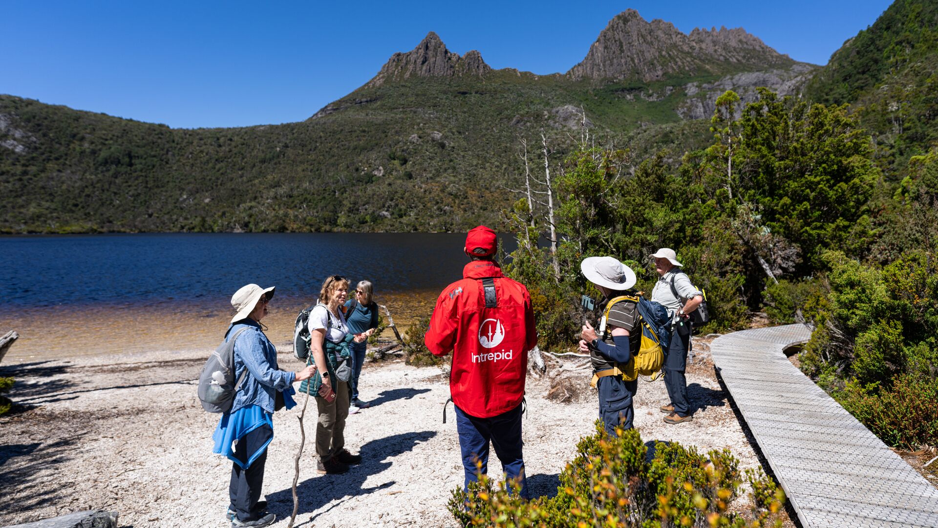 An Intrepid leader talks to a group of travellers about the area while standing on a beach by Cradle Mountain.