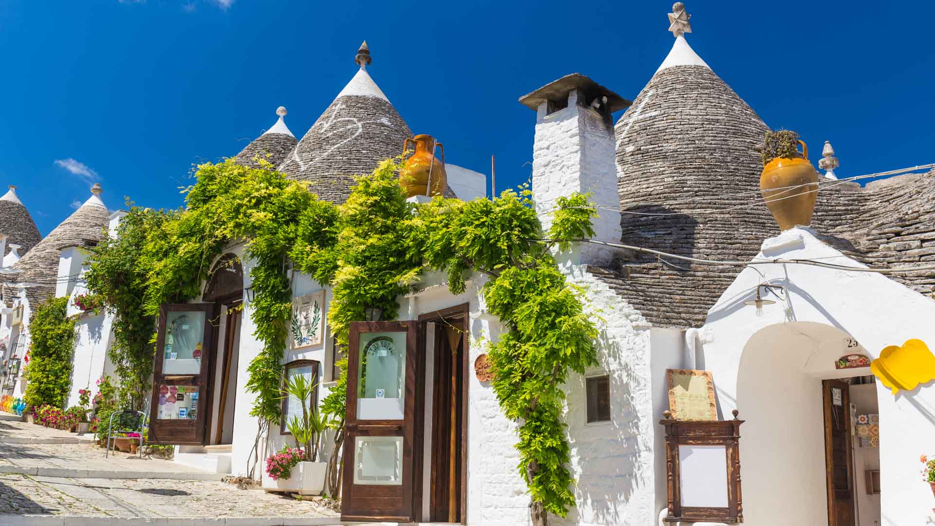 A row of five white houses with conical rooftops is decorated with bright green foliage.