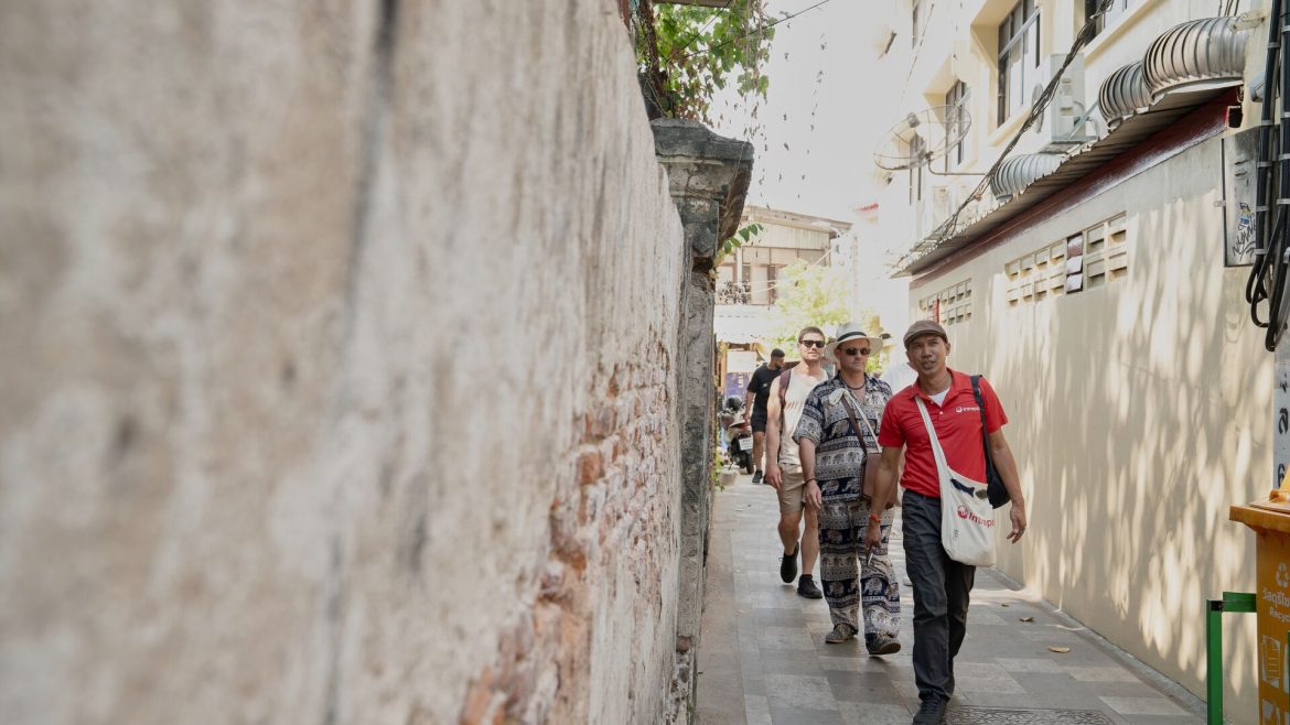 An Intrepid Urban Adventures leader leads a group of travellers down a sun-dappled alleyway in Bangkok