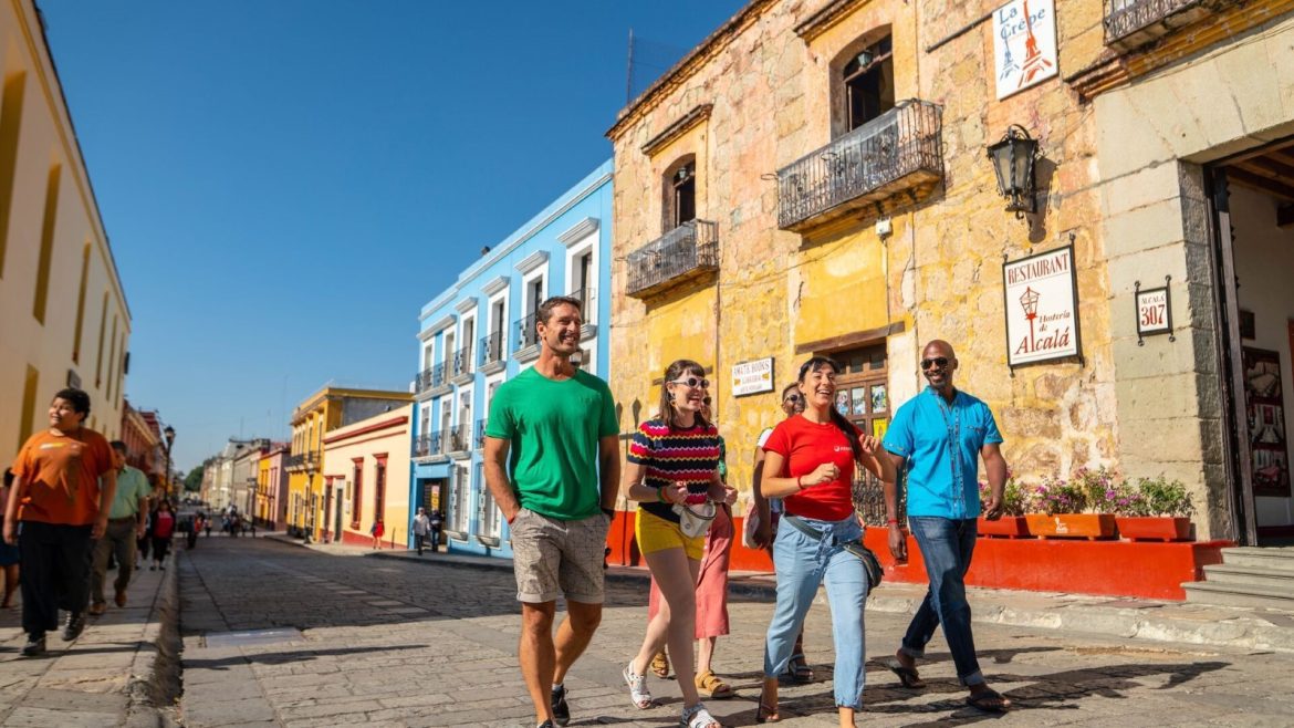 A group of travellers and their Intrepid leader walk through a colourful street in Mexico.