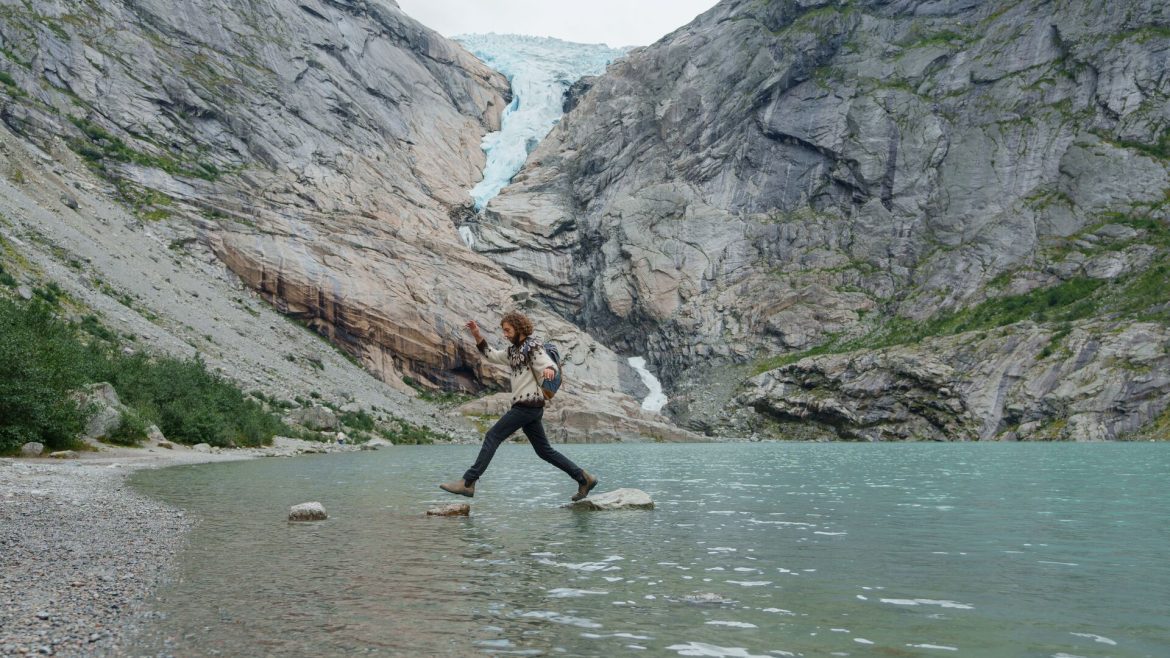 Traveller hopping over stepping stones near a Norwegian glacier