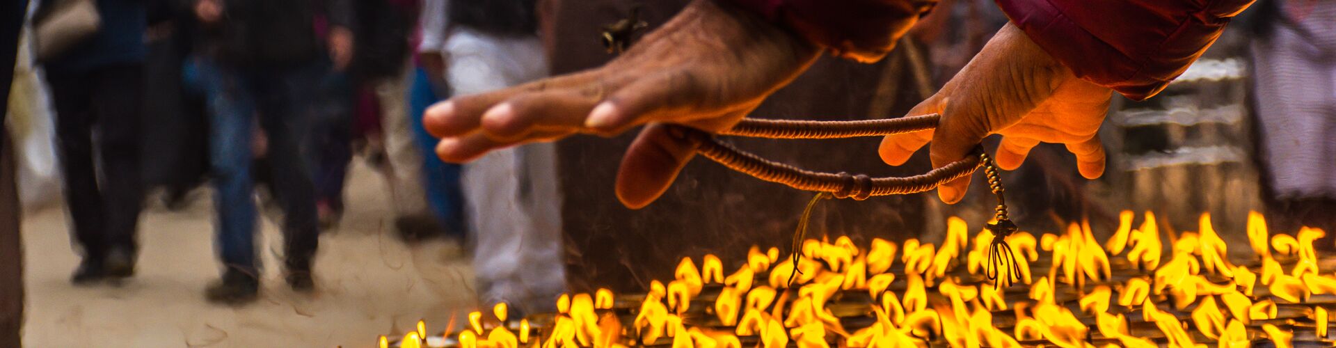 A man warming his hands over butter lamps in Kathmandu, Nepal