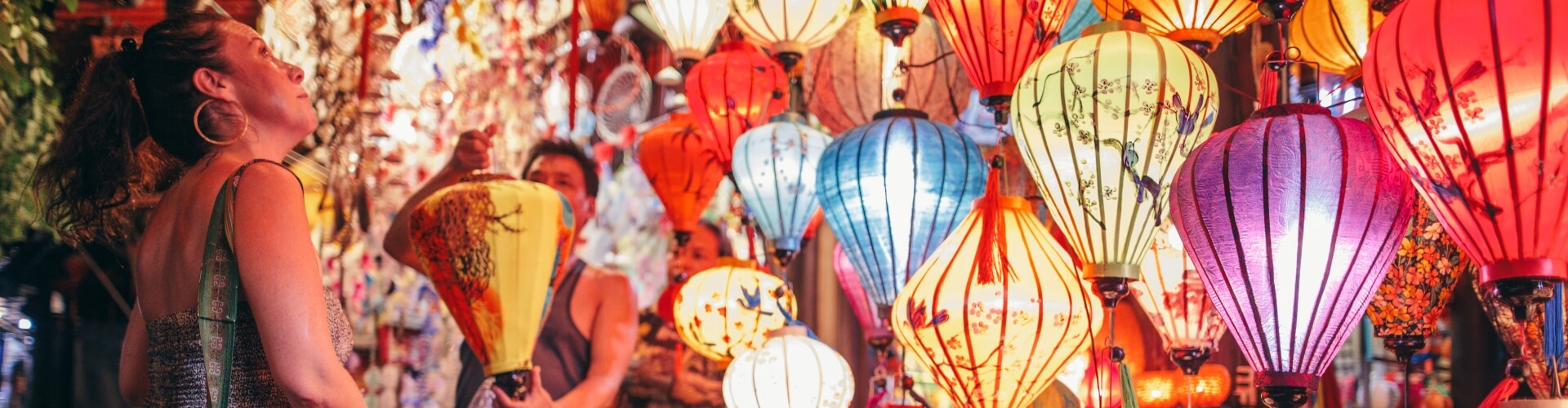 Woman looking at all the brightly coloured lanterns at a shop in Hoi An, Vietnam