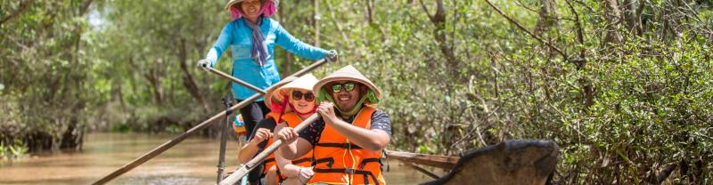 three travellers paddling through mangroves in the Mekong Delta wearing orange lifejackets and Asian hats