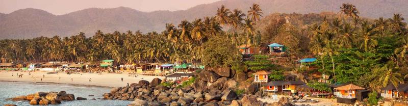 Tropical sunset beach with bungalow and coconut palm trees at Palolem in Goa, India
