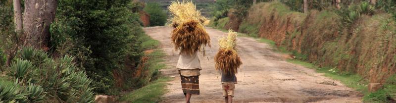 Two local African people walking down a dirt track carrying supplies