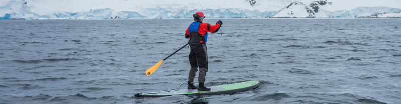 Intrepid traveller mid row while stand-up paddleboarding in ocean of Antarctica
