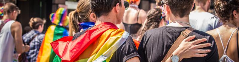 A group of people standing together with a pride, rainbow coloured food around their shoulders.