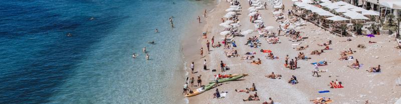 People gathering on a beach in Dubrovnik with many laying on the sand and playing in the water 