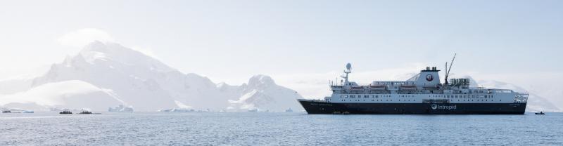 The Ocean Endeavour cruising on gentle Antarctica waters with a looming ice shelf in the distance