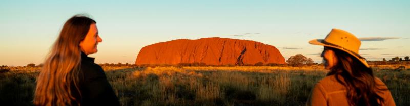 Two travellers admiring Uluru at sunset