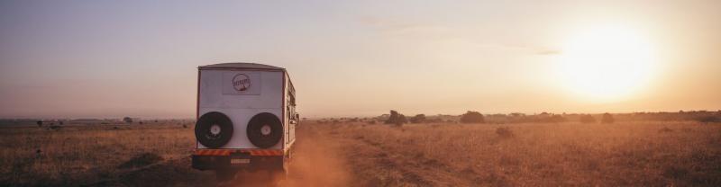 Truck on dirt road driving toward sunset, Kenya