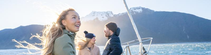 A trio of travelers standing on the deck of a cruise boat during a trip to Milford Sound