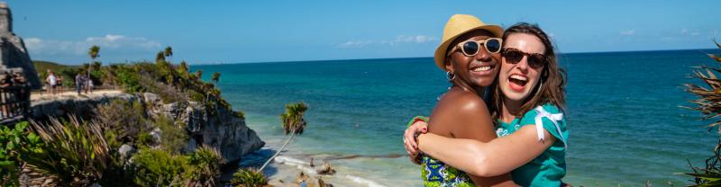 Two similing travelers embrace on a sunny day in Cancun
