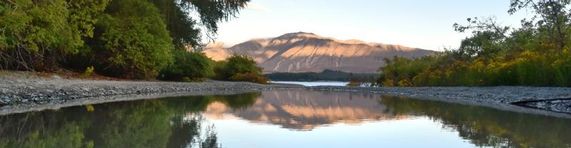 A mirror-like lake reflecting a mountain range in the distance in Tekapo, New Zealand