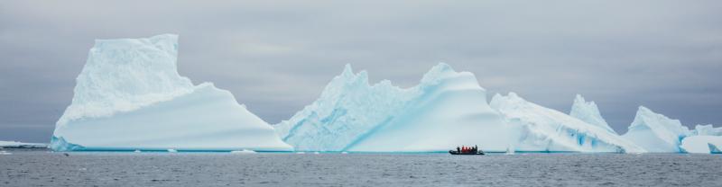 A Zodiac boat cruising in front of a huge iceberg in Antarctica 