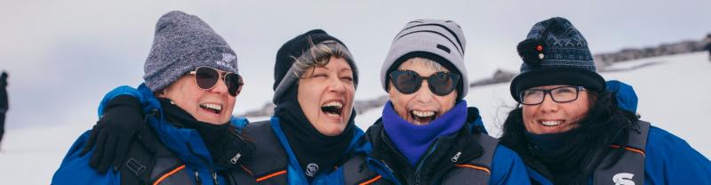 A group of bundled up women laughing and smiling at the camera on their Antarctica cruise