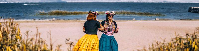 Two travelers dressed in traditional clothing dance on the shores of Lake Titicaca in Peru