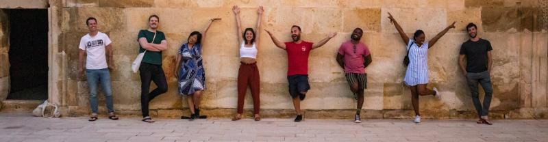 A line of people standing against a wall in varying poses 