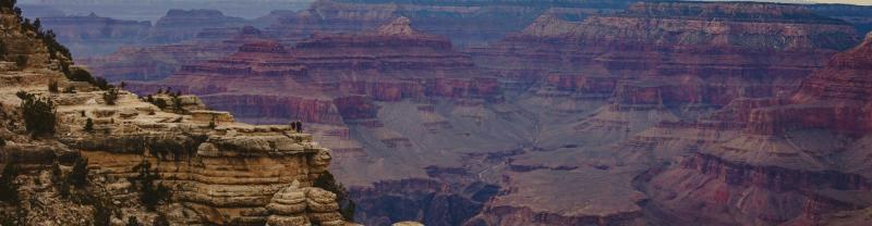 Two travelers standing on a rocky ledge overlooking Grand Canyon National Park in Arizona.