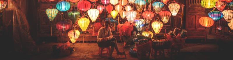 Local lantern seller sitting in front of lit-up lanterns in Hoi An. 