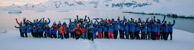 A large group of people cheering at the camera during a site landing in Antarctica