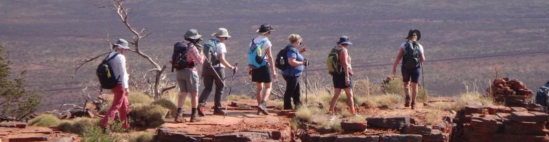 A group of people walking along a mountainous range in Karijini National Park 