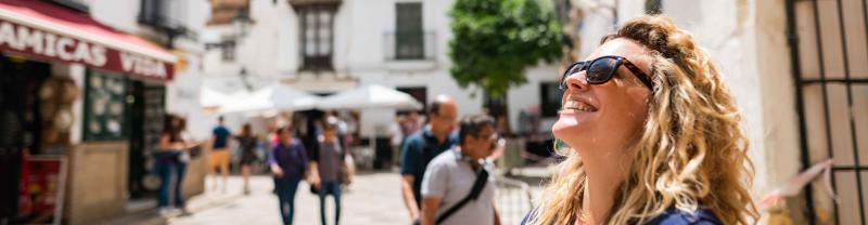 A traveler tips her face to the sun while standing in a piazza in Seville, Spain