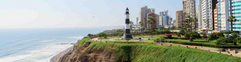 A black and white lighthouse sits in front of the Miraflores skyline outside of Lima, Peru