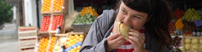 Young traveller eating empanada in front of a fruit stall in Buenos Aires