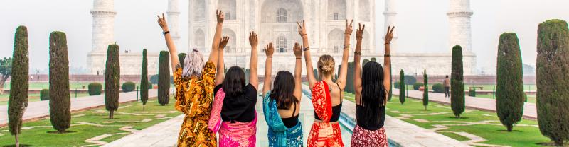 A group of 5 travellers in traditional dress posing in front of India's Taj Mahal