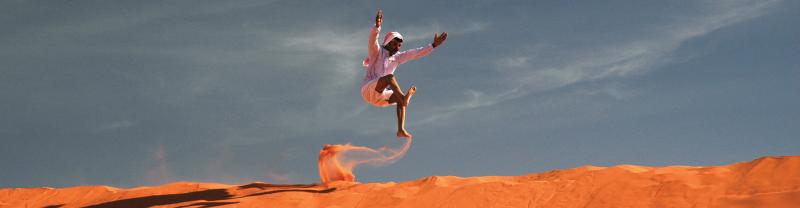 Local man running and jumping on orange sand dune against blue sky