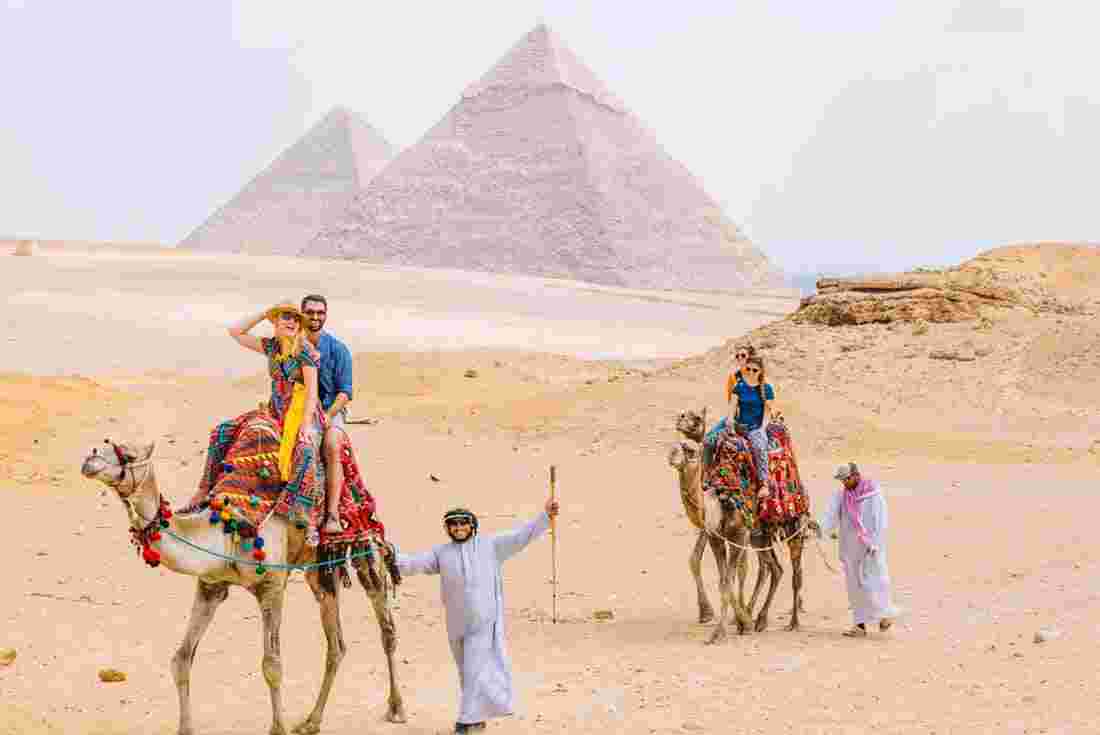 Travellers on camels in Egypt in front of the pyramids