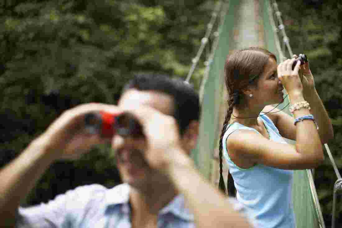 Two people looking through binoculars on a suspension bridge 