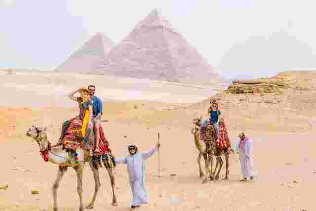 Four travelers riding camels near the Pyramids of Giza in Egypt