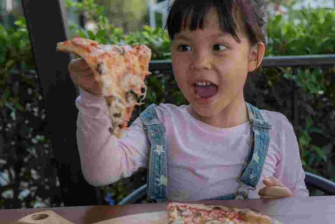 A girl holding up a piece of pizza in Italy with her mouth open 