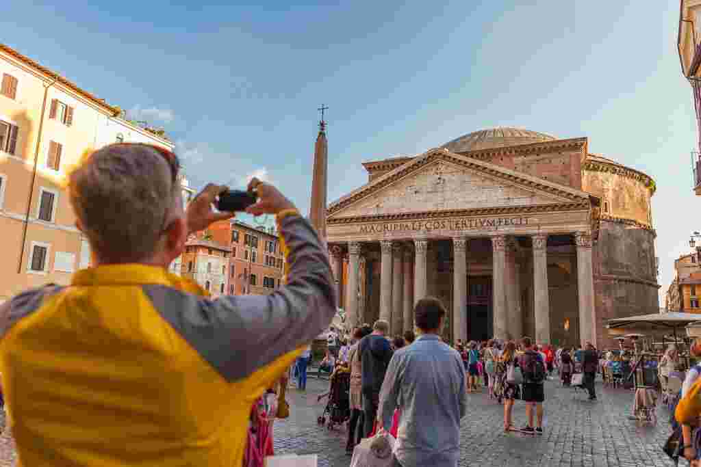 A man captures a photo of the Pantheon in Rome during golden hour.